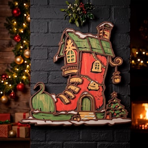 May include: A multi-layered wooden wall decoration shaped like a red boot house with a green roof, arched windows, a chimney, and a small Christmas tree. The design features intricate cutouts, a hanging lantern, and snow-like white accents.