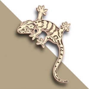 May include: A beige paper cut-out of a gecko with a striped pattern on its back and tail. The gecko is posed with its tail curled up and its head tilted to the side.