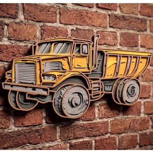 Puede incluir: Una pieza de arte mural de madera multicapa con forma de camión volquete amarillo. El diseño presenta capas de madera superpuestas en tonos amarillos y grises, creando un efecto tridimensional con recortes visibles para las ventanas, la rejilla y las ruedas.
