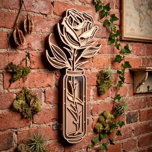 May include: A layered wooden wall art piece featuring a rose flower emerging from a rectangular vase. The design uses stacked light and dark wood tones to create depth, showcasing a stylized floral stem and petals mounted on a brick wall.