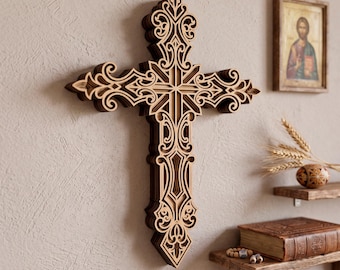 May include: A multi-layered wooden cross featuring intricate laser-cut scrollwork and filigree patterns. The design consists of stacked layers of dark and light wood, creating a three-dimensional effect with ornate, symmetrical decorative details.