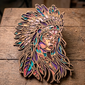 May include: A multi-layered wooden artwork of a Native American woman in a headdress. The piece uses intricate cutouts and is painted with vibrant colours including purple, teal, and peach. The artwork is displayed on a wooden surface.