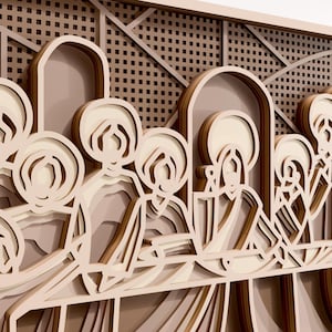 Puede incluir: Una obra de arte de madera en capas que representa una escena religiosa. La obra presenta figuras con halos, sentadas a una mesa. La pieza está hecha de madera de color marrón claro y crema, con un diseño detallado y dimensional.