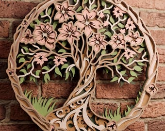 May include: A circular multi-layered wooden wall art piece featuring a tree with light pink flowers and sage green leaves. The intricate design is composed of stacked cutouts creating depth, with a brown frame enclosing the tree motif.