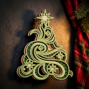 May include: A layered wooden wall decoration shaped like a stylized Christmas tree. The design features swirling, organic curves in shades of light and dark green with natural wood edges. Several eight-pointed star cutouts are integrated throughout.