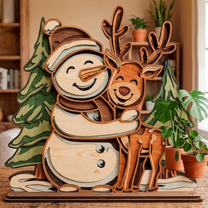 Peut inclure: Décoration de Noël en bois représentant un bonhomme de neige étreignant un renne. Le bonhomme de neige porte un chapeau et une écharpe, et le renne a des bois. La conception en couches crée un effet 3D. La palette de couleurs comprend des nuances de marron, beige et vert.