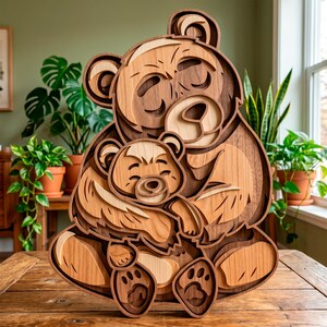 Könnte beinhalten: Mehrschichtige Holzskulptur einer Bärenmutter, die ein Baby umarmt. Das Kunstwerk besteht aus verschiedenen Brauntönen, mit detaillierten Gesichtern und Pfoten. Auf einem Holztisch platziert, mit Pflanzen im Hintergrund.