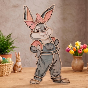 May include: A multi-layered wooden cutout of a cartoon rabbit wearing overalls and a bow. The rabbit features shades of gray, pink, and cream, with a textured wood grain finish. The design is composed of stacked layers creating a 3D effect.