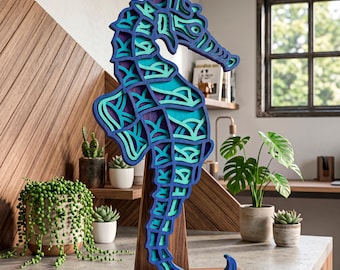 Könnte beinhalten: Eine mehrschichtige Holzskulptur eines Seepferdchens in Blau-, Türkis- und Lilatönen, montiert auf einem Holzsockel. Das Seepferdchen ist aufwendig mit einem detaillierten Design geschnitten. Die Skulptur wird auf einer Arbeitsplatte mit Pflanzen im Hintergrund ausgestellt.