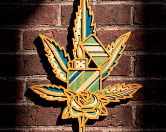 Puede incluir: Adorno de pared de madera con un diseño de hoja de cannabis con un encendedor y una rosa. La obra de arte está superpuesta con tonos de amarillo, verde y azul, y cuelga contra una pared de ladrillo. El diseño mide unos 30 cm de altura.