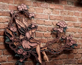 May include: A multi-layered wooden wall art piece featuring a fairy with wings sitting on a flowering branch. The design incorporates shades of soft pink, muted brown, and dark charcoal, creating a dimensional effect with intricate cutouts of blossoms and leaves.