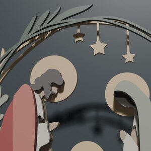 May include: A layered wooden nativity scene featuring stylized figures of two adults and a child under a circular arch decorated with leaves and hanging stars. The figures are rendered in muted tones of beige, gray, and dusty rose with circular halos.