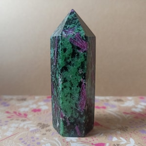 Può includere: Una punta di cristallo verde e viola, nota anche come pietra preziosa, con una cima appuntita e una base piatta. Il cristallo è lucido e ha una superficie liscia.