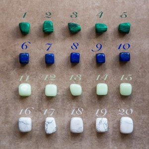 以下が含まれることがあります： 20個の番号が付けられた、研磨された、丸みを帯びた石がグリッドパターンで配置されています。石は緑、青、薄い緑、白の4色です。石は5列に並んでいます。