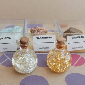 May include: Three small glass bottles with cork stoppers filled with gold and silver flakes. The bottles are labelled "Ludwigita Italia", "Vanadinita Marruecos", and "Granate Madagascar".