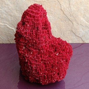 May include: A large, bright red coral specimen with a unique, intricate, and textured surface. The coral is shaped like a heart and has a rough, porous texture.