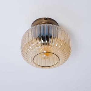 May include: A gold ceiling light fixture with a clear, amber-coloured glass shade. The shade has a ribbed design and a round shape.