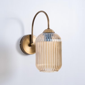 Op de afbeelding: Een messing wandlamp met een gebogen arm en een geribbelde amberkleurige glazen kap.