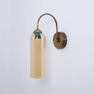 May include: A brass wall sconce with a curved arm and a ribbed amber glass shade.
