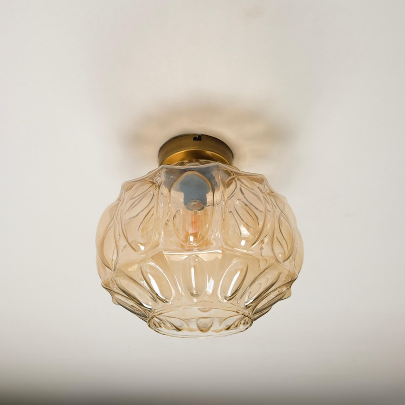 May include: A vintage-style ceiling light fixture with a clear, amber-colored glass shade. The shade has a textured, floral pattern and is attached to a brass-colored base. The light bulb is visible inside the shade.