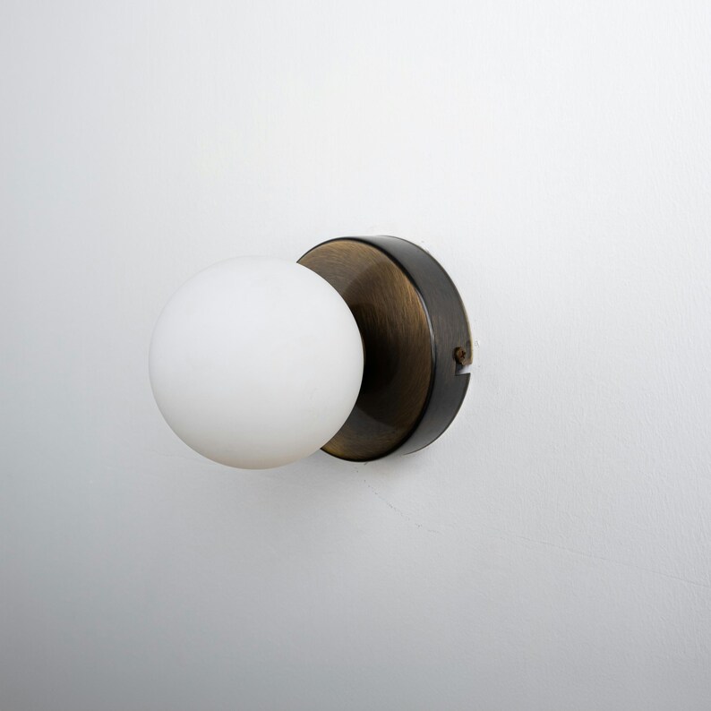 Op de afbeelding: Een witte bolvormige lamp met een zwarte en messing wandbevestiging.