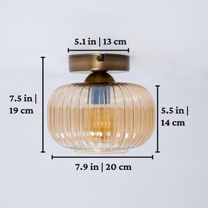 May include: A gold ceiling light fixture with a ribbed amber glass shade. The fixture measures 7.5 inches tall, 5.5 inches wide, and 7.9 inches in diameter.