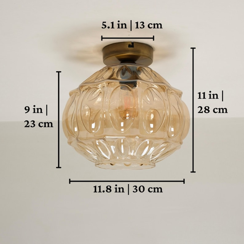 May include: A vintage-style ceiling light fixture. The fixture is 11 inches (28 cm) tall and 11.8 inches (30 cm) wide, with a 9-inch (23 cm) diameter. It features a bronze-colored base and a clear, amber-colored glass shade.