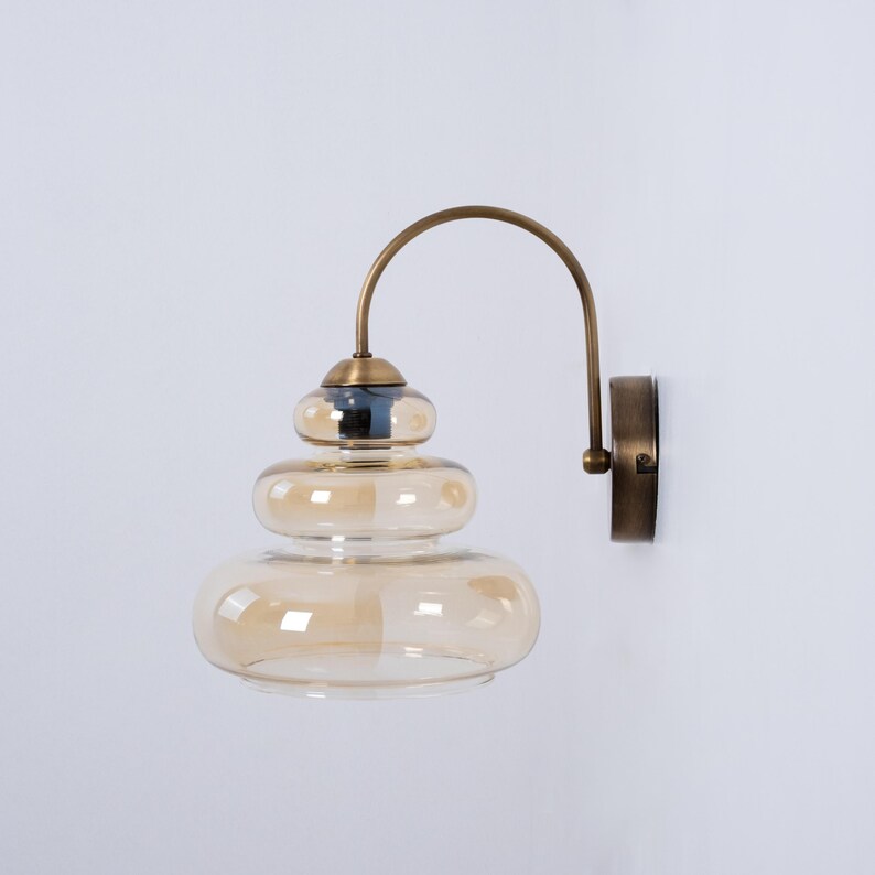 May include: A brass wall sconce with a layered amber glass shade. The sconce has a curved arm and a round base.