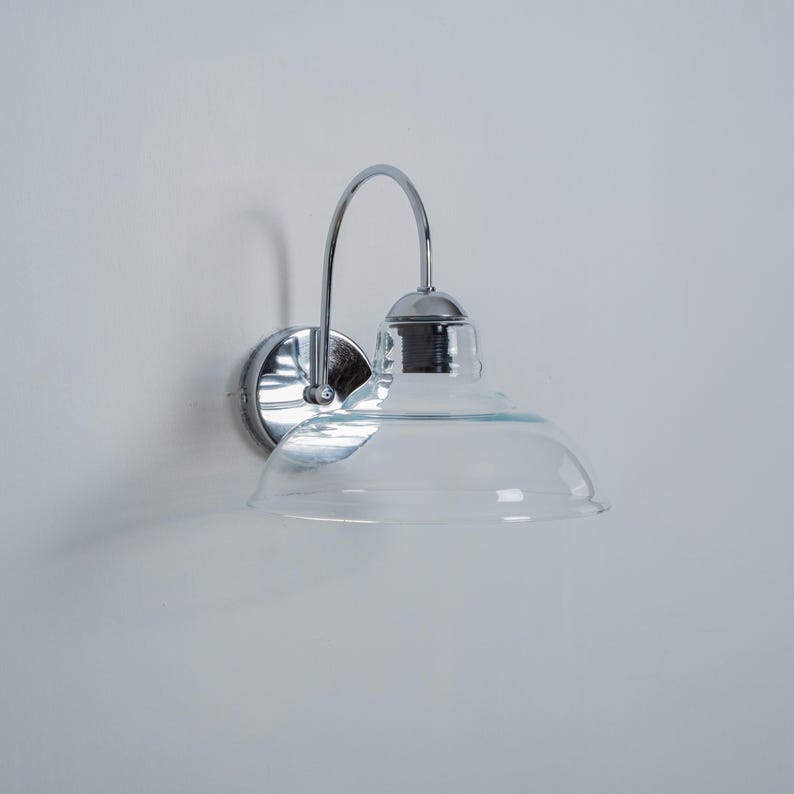May include: A chrome wall sconce with a clear glass shade. The sconce has a curved arm and a round base.