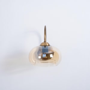 May include: A brass wall sconce with a round, amber glass shade. The sconce has a simple, elegant design.