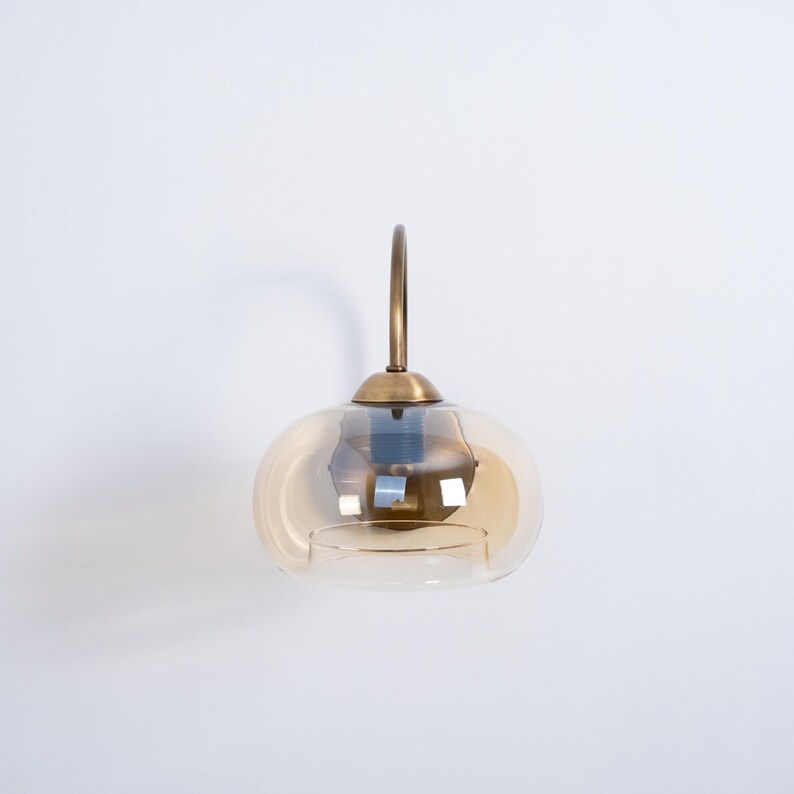 May include: A brass wall sconce with a round, amber glass shade. The sconce has a simple, elegant design.
