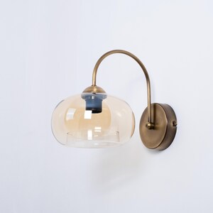 May include: A brass wall sconce with a curved arm and a round amber glass shade.