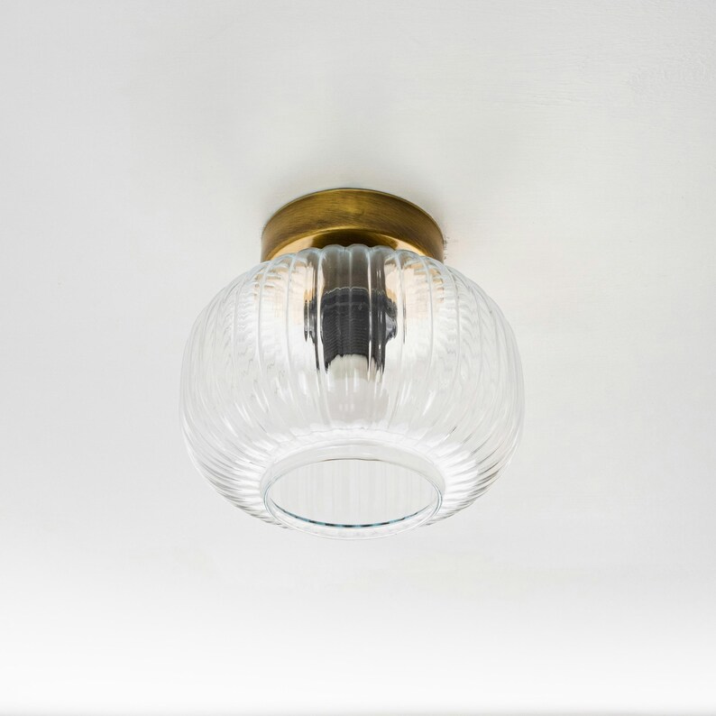 Op de afbeelding: Een plafondlamp van helder glas met een messing afwerking. Het glas heeft een geribbelde textuur en is koepelvormig.