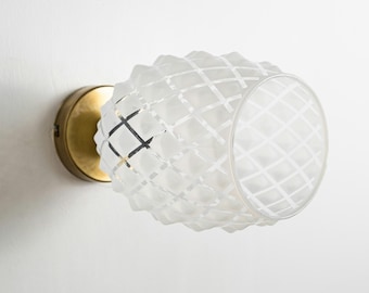 May include: A white frosted glass wall sconce with a geometric pattern and a brass base.