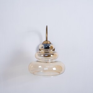 May include: A gold wall sconce with a layered amber glass shade. The sconce has a curved arm and a simple design.