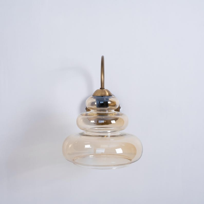 May include: A gold wall sconce with a layered amber glass shade. The sconce has a curved arm and a simple design.