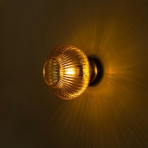 Op de afbeelding: Een gouden wandlamp met een geribbelde glazen kap die een warm, geel licht uitstraalt.