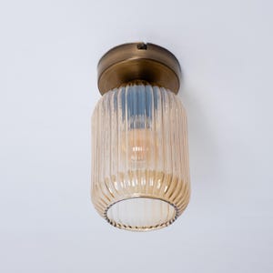 Op de afbeelding: Een messing plafondlamp met een geribbelde amberkleurige glazen kap.