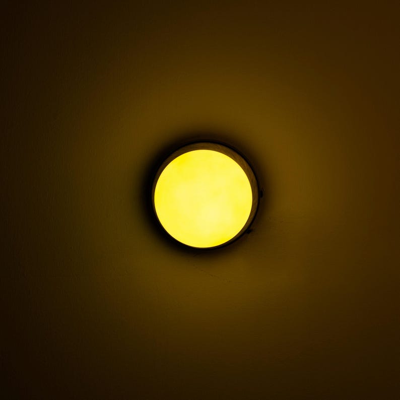 Op de afbeelding: Een ronde plafondlamp met een geel licht dat schijnt door een witte diffuser.