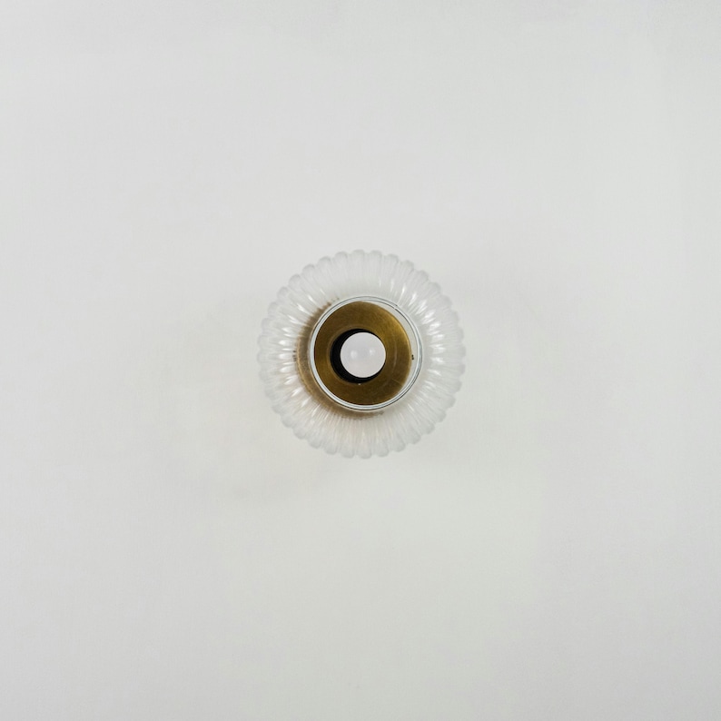 Op de afbeelding: Een glazen lampenkap van helder glas met een geribbelde textuur en een messing middenring. De lampenkap is rond en heeft een witte achtergrond.