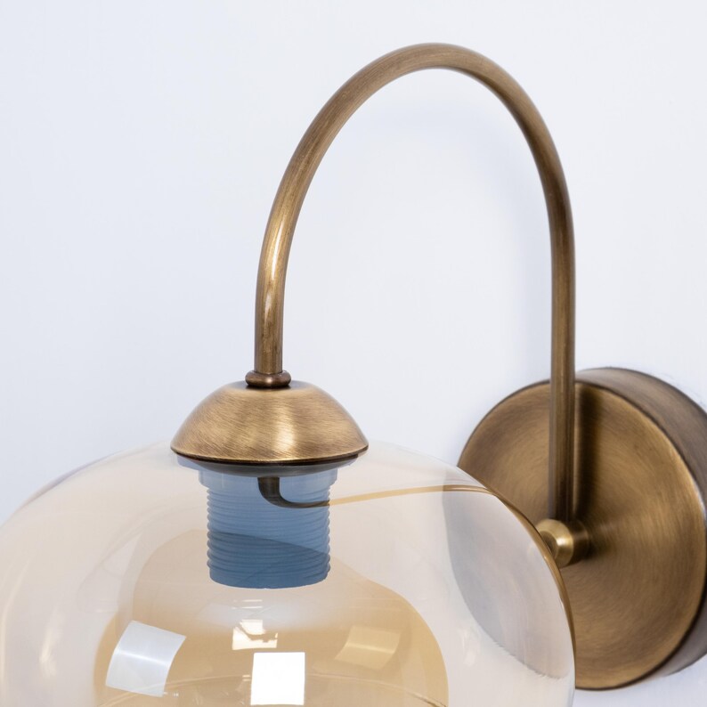 May include: A brass wall sconce with a curved arm and a round amber glass shade.