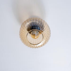 May include: A round, amber-colored glass ceiling light fixture with a ribbed texture. The light is on and illuminates the room.