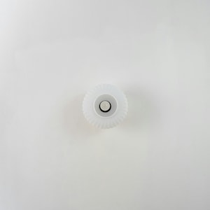 Op de afbeelding: Witte plastic flesdop met een geribbelde rand en een klein, rond, wit midden.