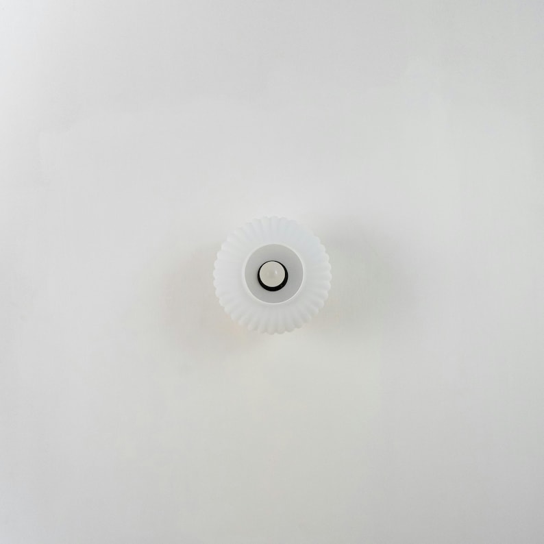 Op de afbeelding: Witte plastic flesdop met een geribbelde rand en een klein, rond, wit midden.