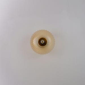 K&ouml;nnte beinhalten: Eine wei&szlig;e Glasleuchte mit geripptem Design. Die Leuchte hat eine runde Form und einen goldfarbenen Metallsockel.