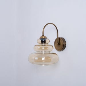 May include: A brass wall sconce with a layered amber glass shade. The sconce has a curved arm and a round wall plate.