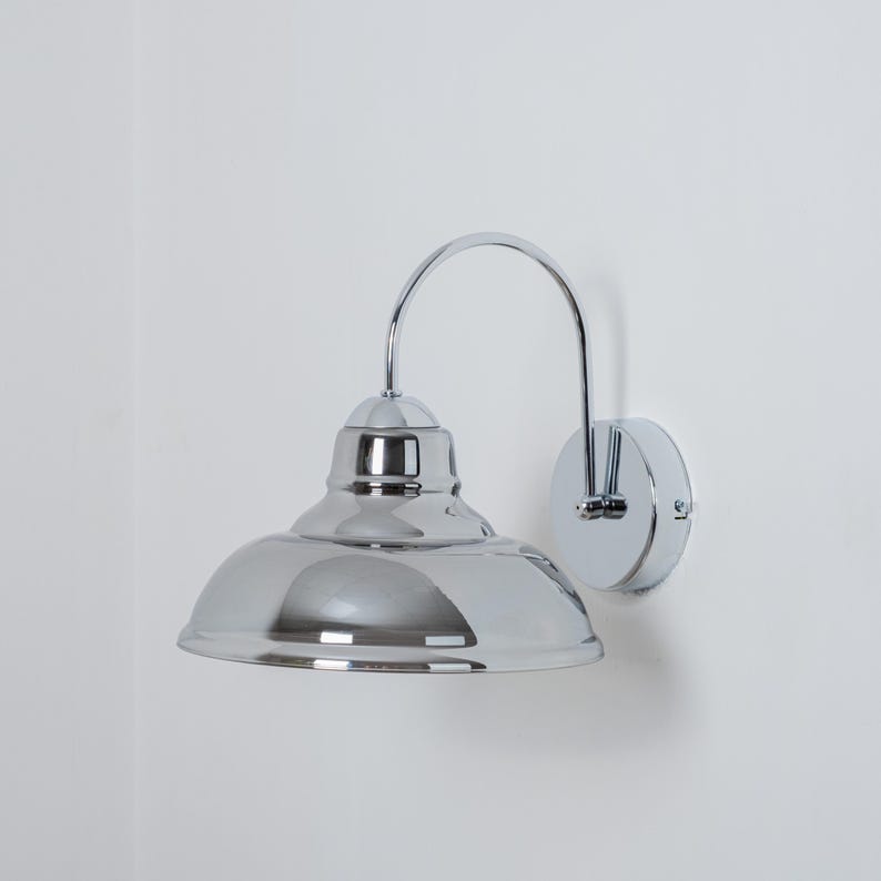 May include: A chrome wall sconce with a curved arm and a round, dome-shaped shade.