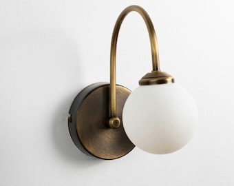 May include: A brass wall sconce with a curved arm and a frosted glass globe. The sconce has a brushed brass finish and a round base.