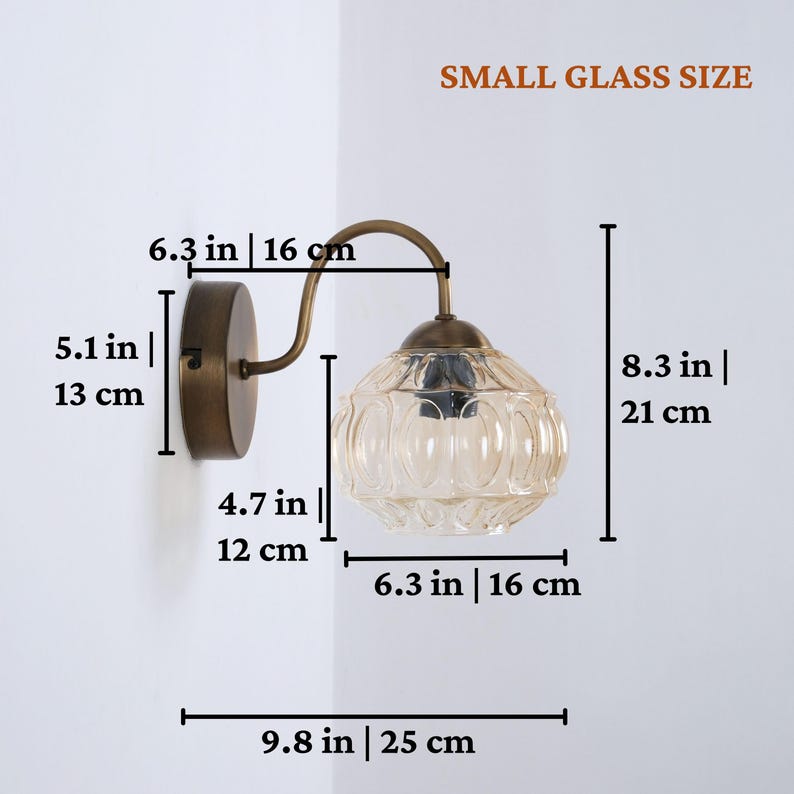 Puede incluir: L&aacute;mpara de pared con acabado bronce y una peque&ntilde;a pantalla de cristal estampada. La l&aacute;mpara mide 25 cm de ancho y 21 cm de alto. El texto "SMALL GLASS SIZE" es visible.