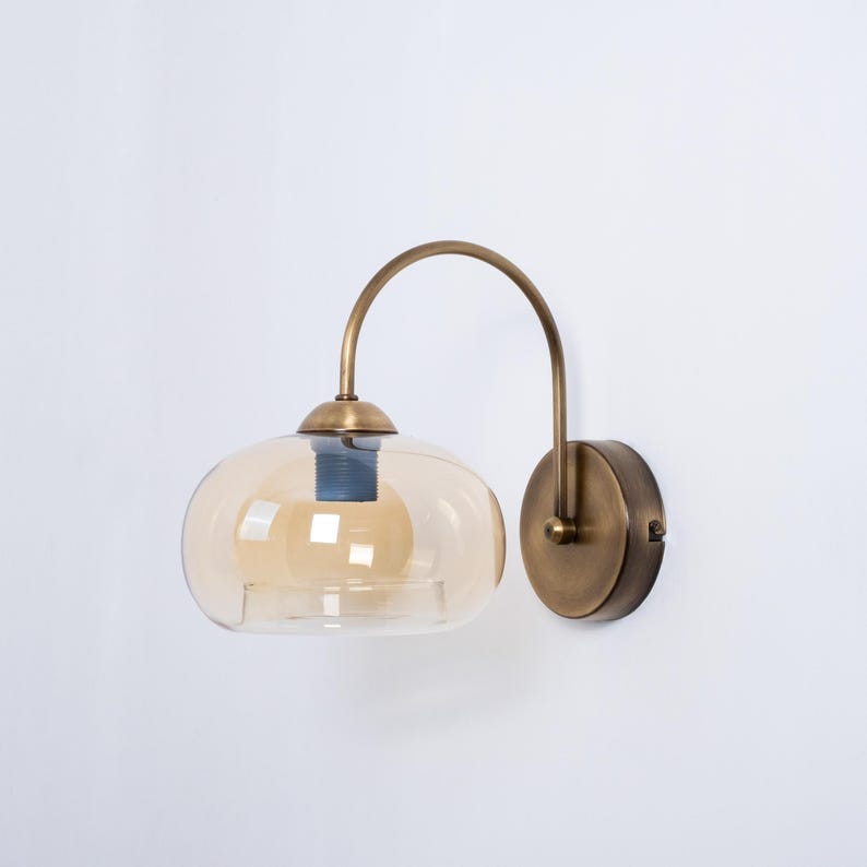 May include: A brass wall sconce with a curved arm and a round amber glass shade.